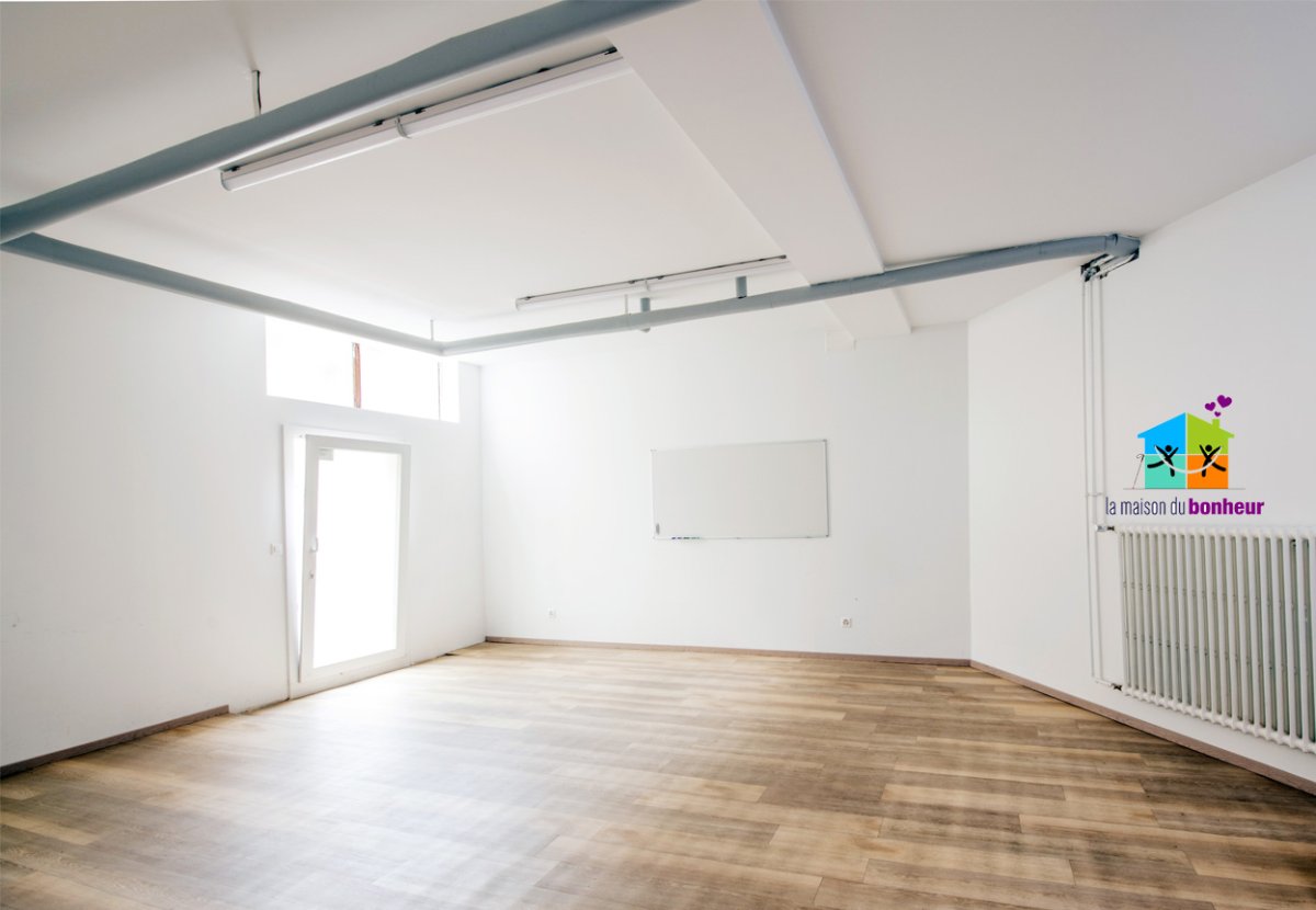 Salle polyvalente Photo de la salle polyvalente dans sa longueur, avec la porte fenêtre à gauche, le panneau d'affichage au fond